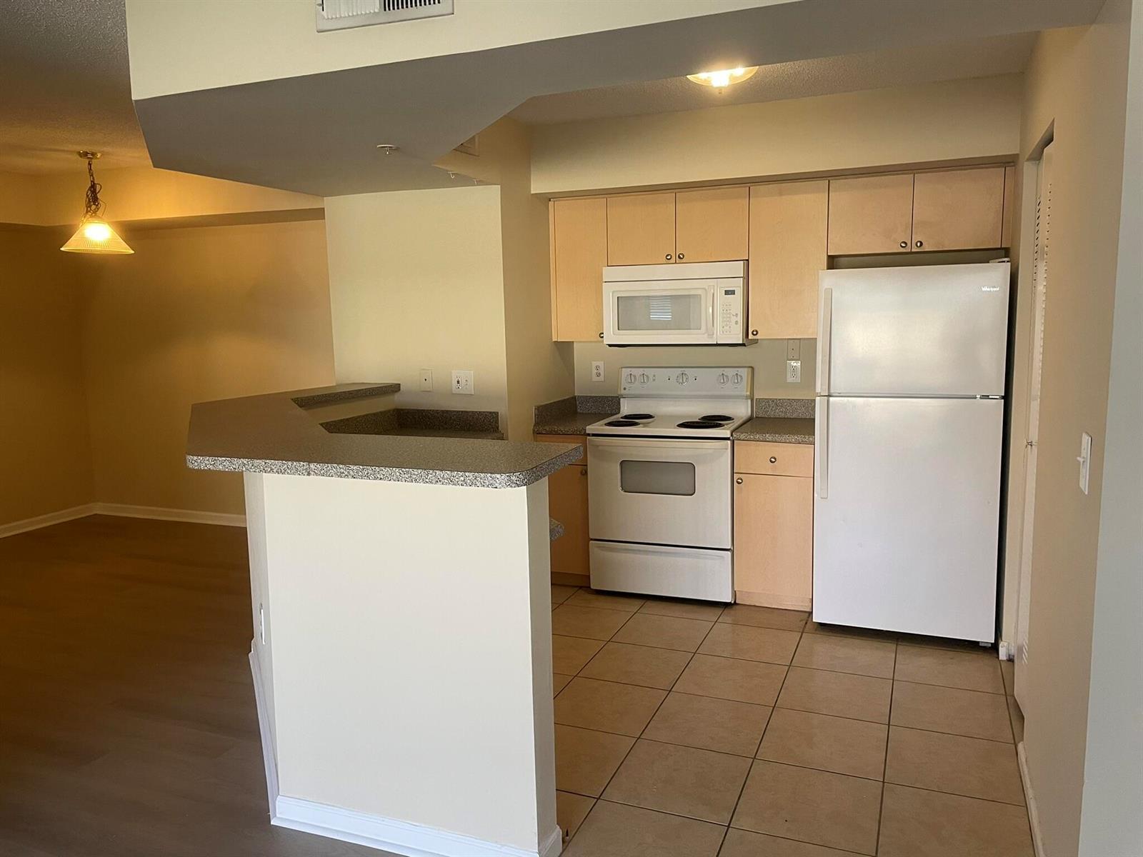 A kitchen with light wood cabinets, white appliances, and a breakfast bar overlooking a room — 3605 NW Adriatic Lane # 103, Jensen Beach FL 34957, JENSEN BEACH, FL