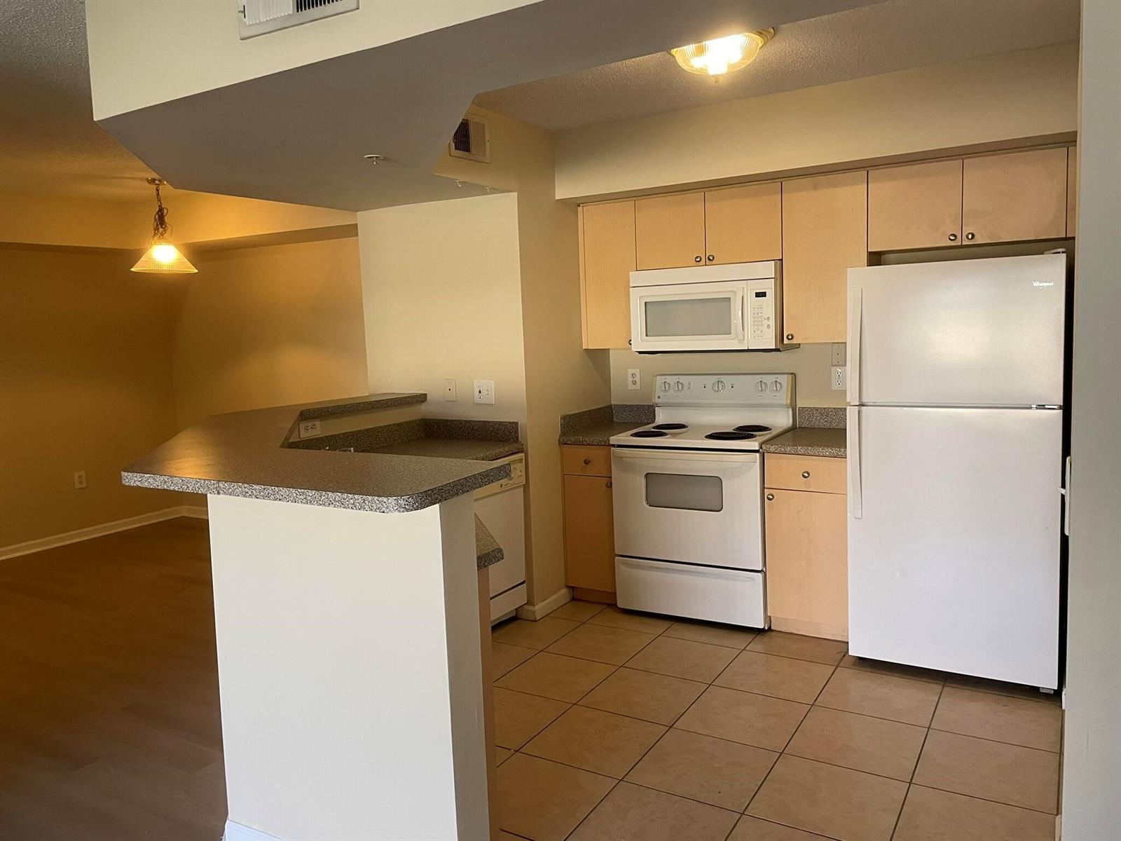 A kitchen with light wood cabinets, white appliances, and a breakfast bar overlooking a room — 3605 NW Adriatic Lane # 103, Jensen Beach FL 34957, JENSEN BEACH, FL