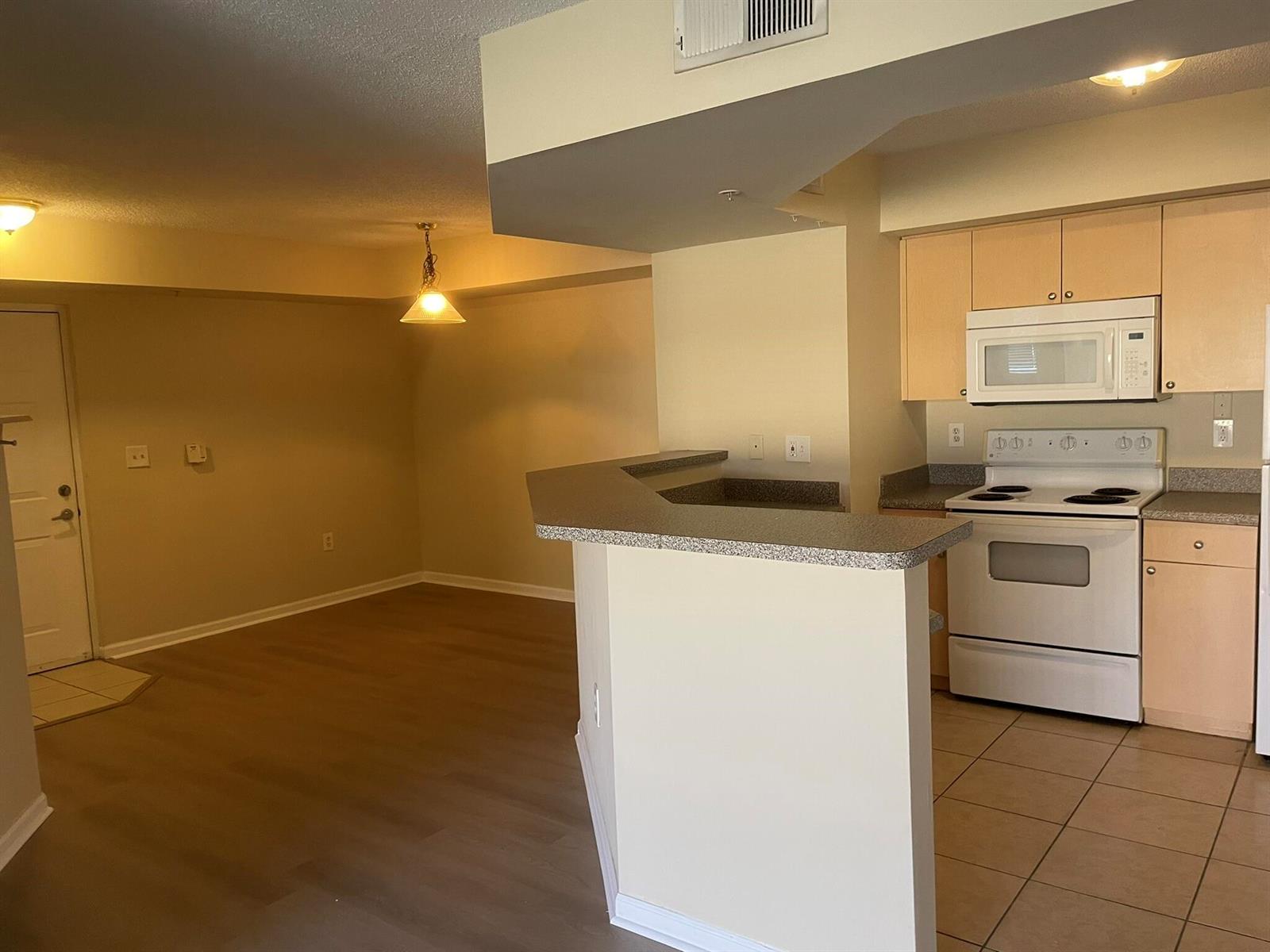 An open-concept kitchen with light wood cabinets and a breakfast bar overlooks a dining area — 3605 NW Adriatic Lane # 103, Jensen Beach FL 34957, JENSEN BEACH, FL
