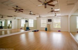 A spacious fitness studio with light wood flooring, mirrored walls, and multiple ceiling fans — 3957 Cranesbill Court, FL 33920, FL