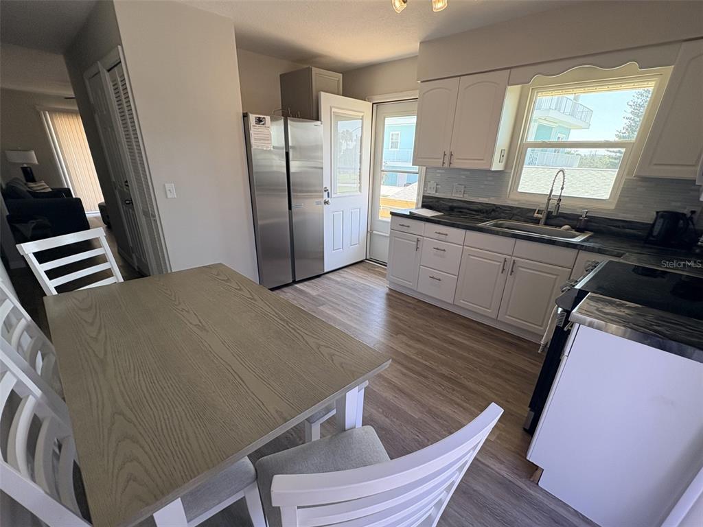 A kitchen features white cabinets, stainless steel appliances, a dining table, and wood-look flooring — 6693 ENGRAM ROAD, NEW SMYRNA BEACH, FL