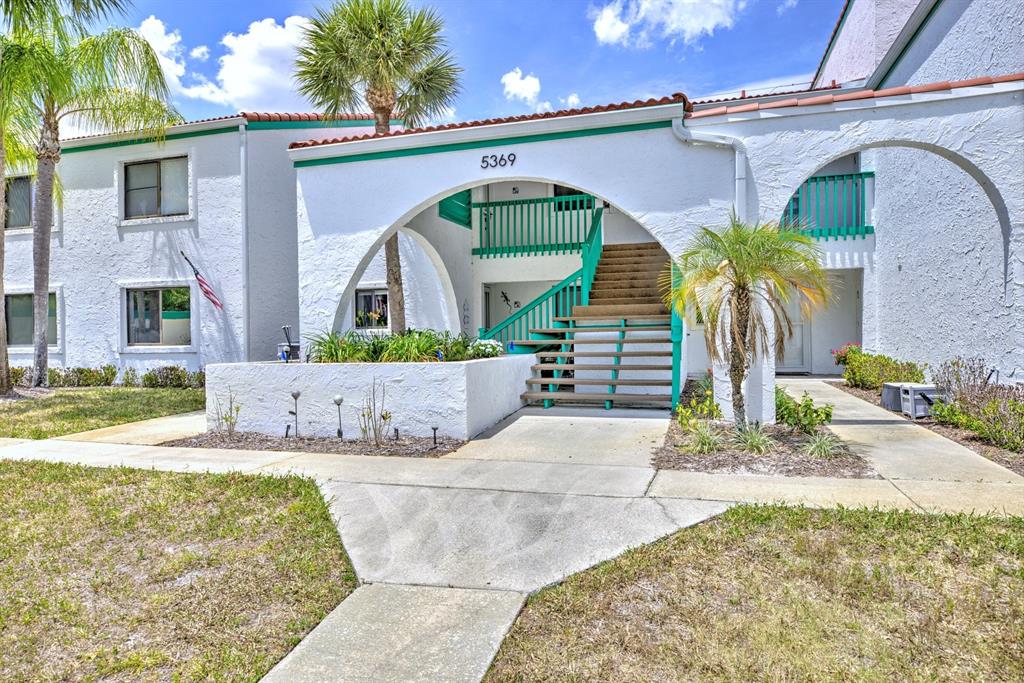 A two-story white stucco apartment building features a central arched entryway with wooden stairs — 5369 CASABLANCA CIRCLE UNIT K24, SEBRING, FL