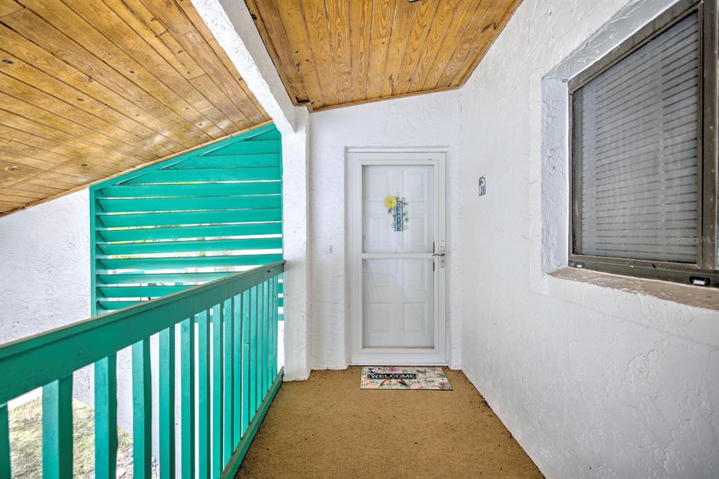 A covered entryway features a white storm door, a teal railing, and wood-paneled ceilings — 5369 CASABLANCA CIRCLE UNIT K24, SEBRING, FL