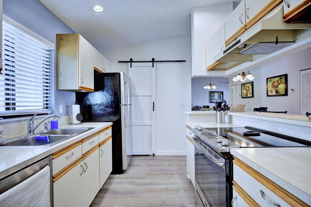 A kitchen features white cabinets with wood trim, stainless steel appliances, and a sliding barn door — 5369 CASABLANCA CIRCLE UNIT K24, SEBRING, FL