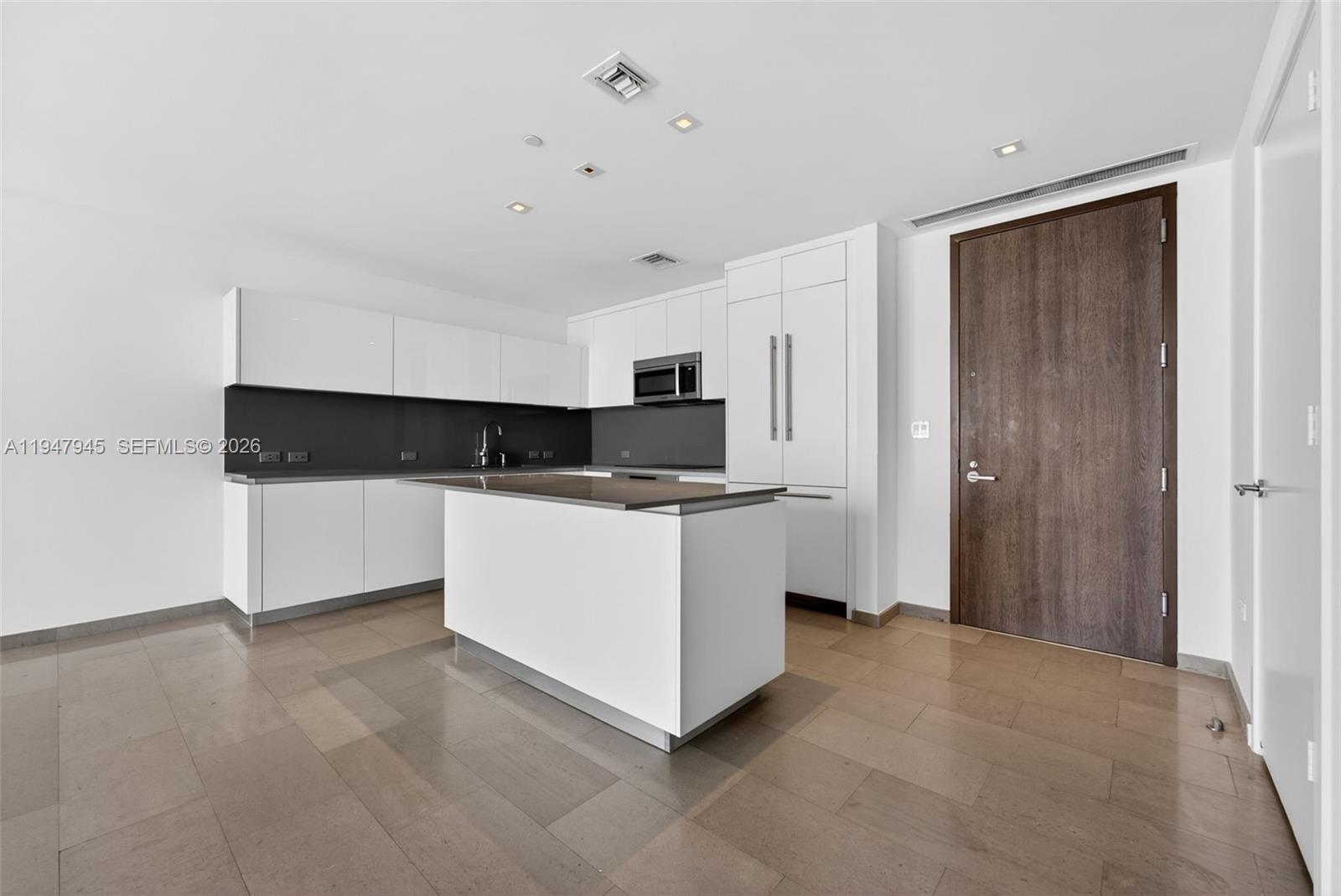 A modern kitchen features white cabinetry, a central island, and dark countertops on tile flooring — 68 SE 6th St # 2110, Miami FL 33131, MIAMI, FL