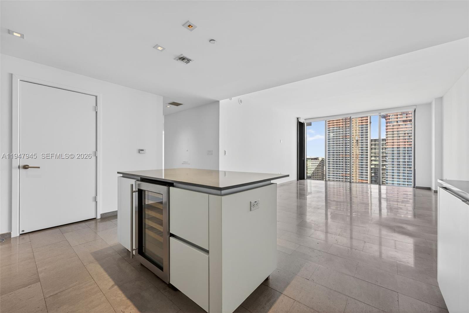 A modern kitchen island with a wine cooler sits in a bright, open-plan apartment — 68 SE 6th St # 2110, Miami FL 33131, MIAMI, FL