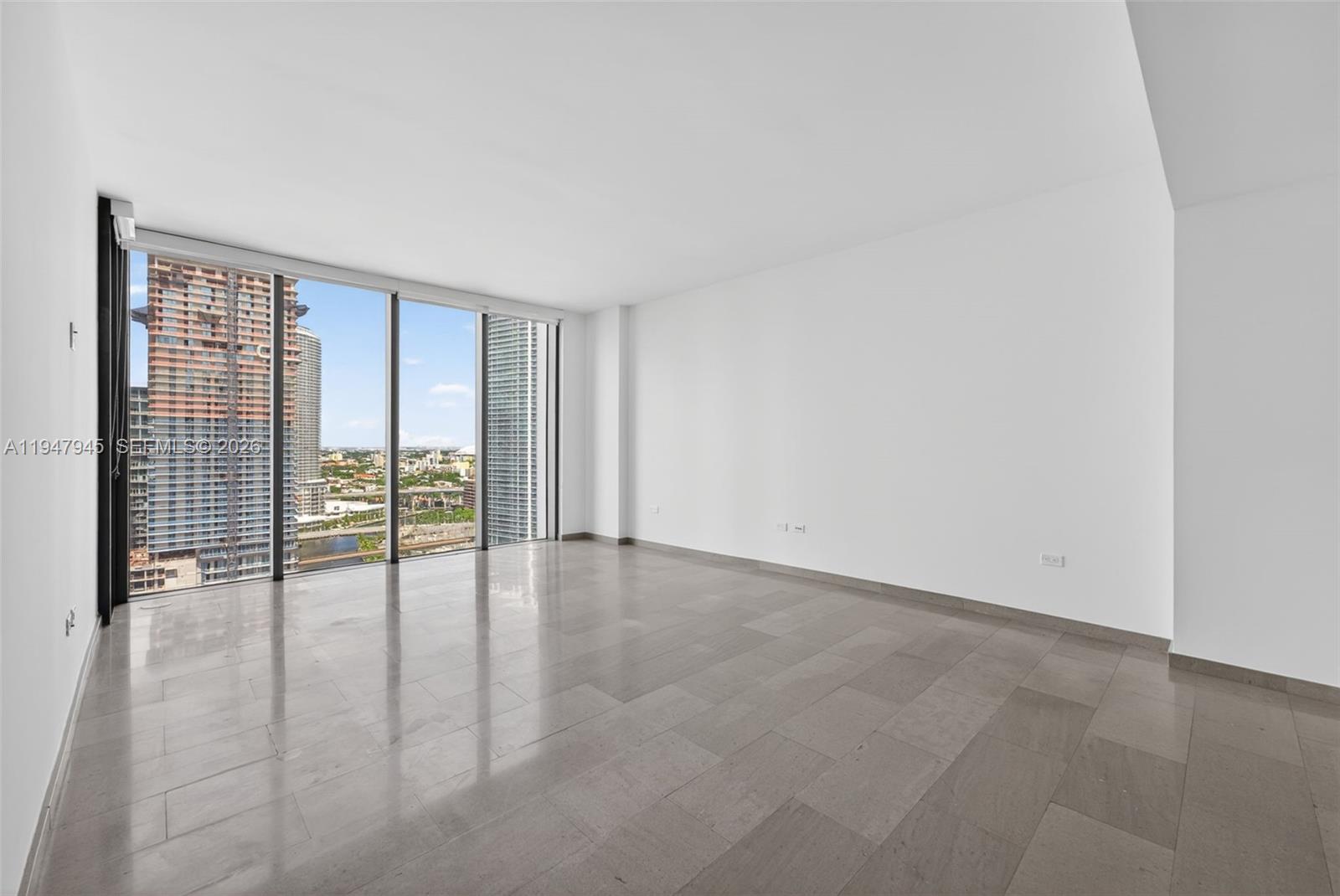 An empty room with white walls, gray tile flooring, and floor-to-ceiling windows overlooking city buildings — 68 SE 6th St # 2110, Miami FL 33131, MIAMI, FL