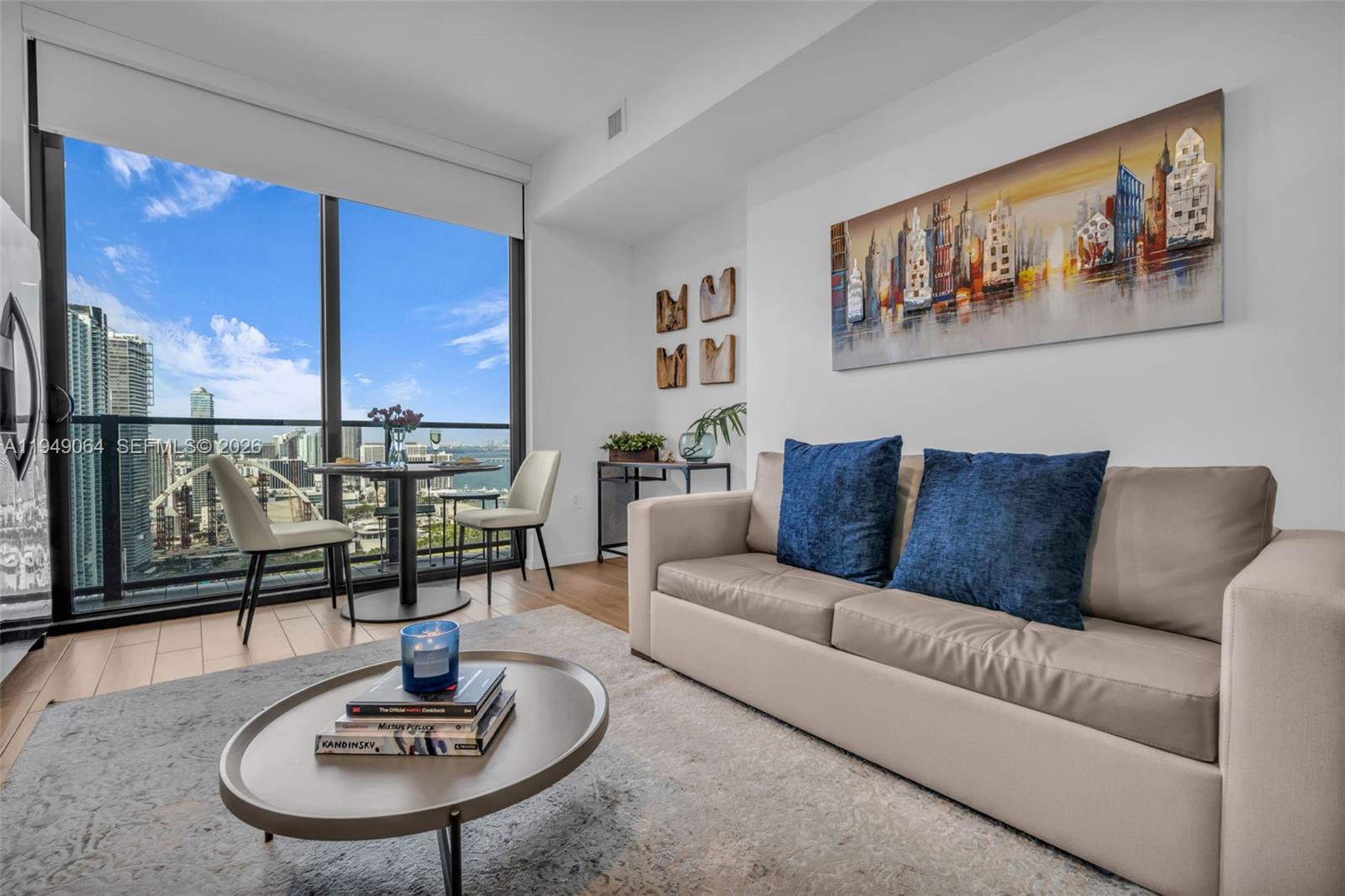 A living room features a beige sofa, a coffee table, and a dining area overlooking a city — 398 NE 5th St # 3207, Miami FL 33132, MIAMI, FL