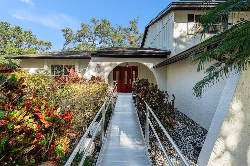 A metal ramp with railings leads to the red front door of a white house — 4611 LANDSCAPE DRIVE, TAMPA, FL
