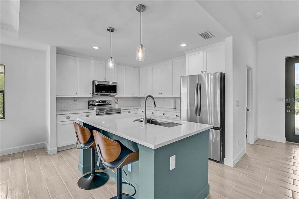 A kitchen features white cabinetry, a teal island with bar stools, and stainless steel appliances — 112 HERCULES DRIVE, ROTONDA WEST, FL
