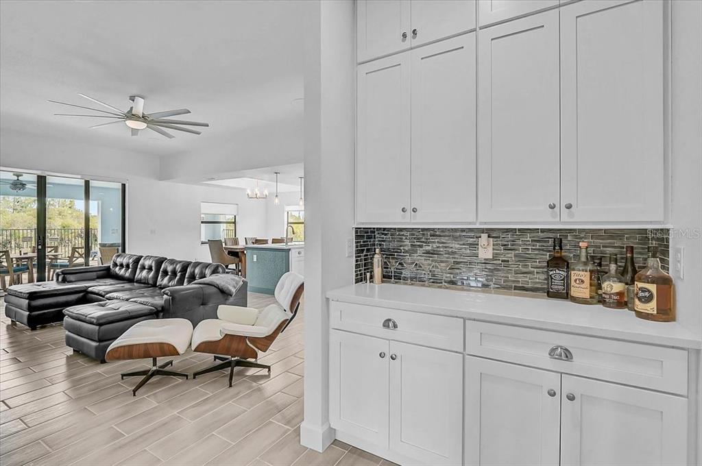 A white kitchen bar area with a tiled backsplash overlooks a living room with furniture — 112 HERCULES DRIVE, ROTONDA WEST, FL