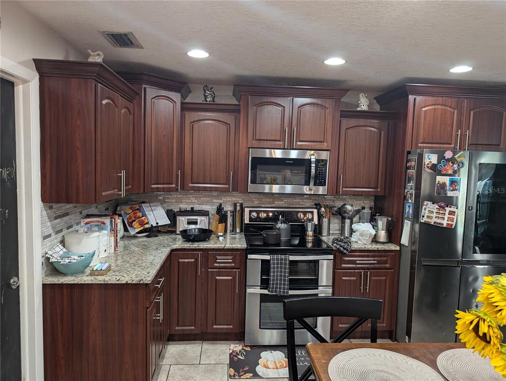 A kitchen features dark wood cabinets, granite countertops, stainless steel appliances, and a tiled backsplash — 4208 SUMMERDALE DRIVE, TAMPA, FL