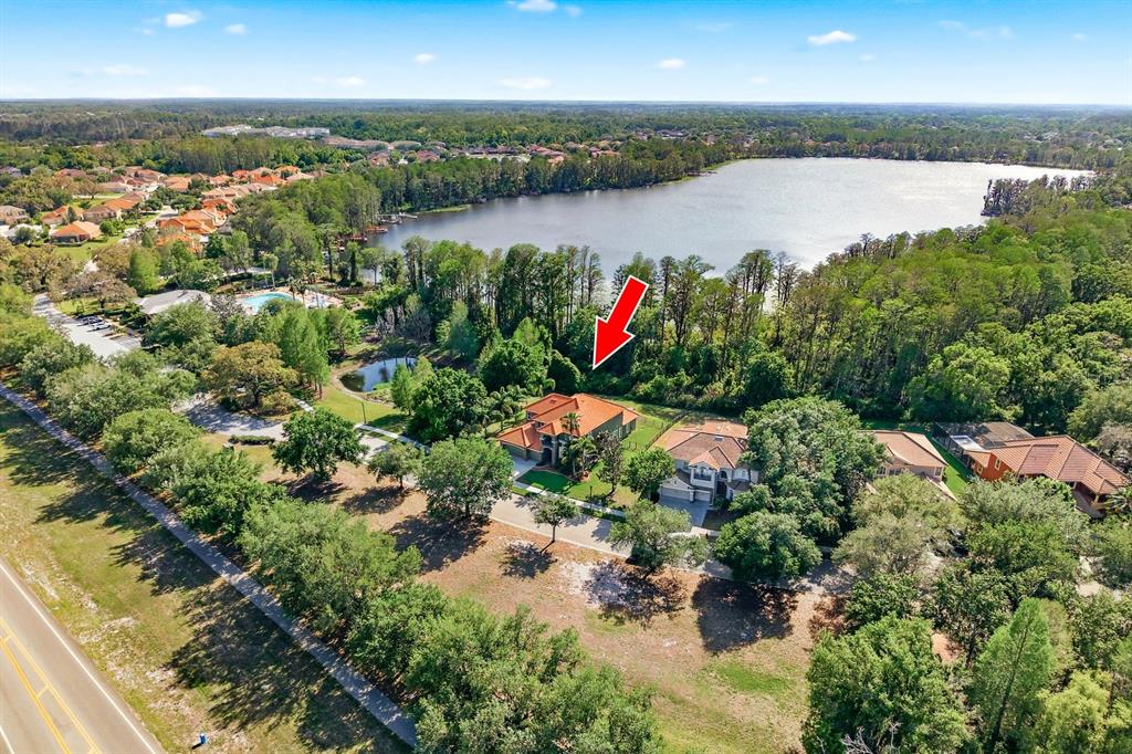 An aerial view shows a house with a red roof near a lake and trees — 9103 CREEDMOOR LANE, NEW PORT RICHEY, FL