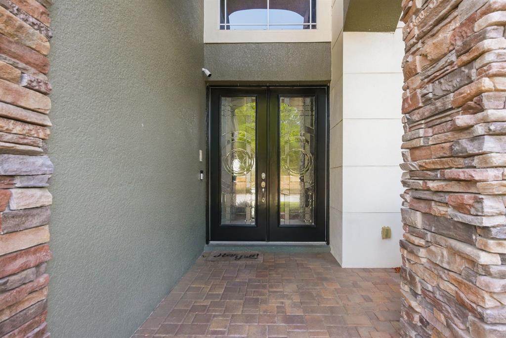 A double front door with glass inserts sits between stone-clad pillars on a paved porch — 9103 CREEDMOOR LANE, NEW PORT RICHEY, FL