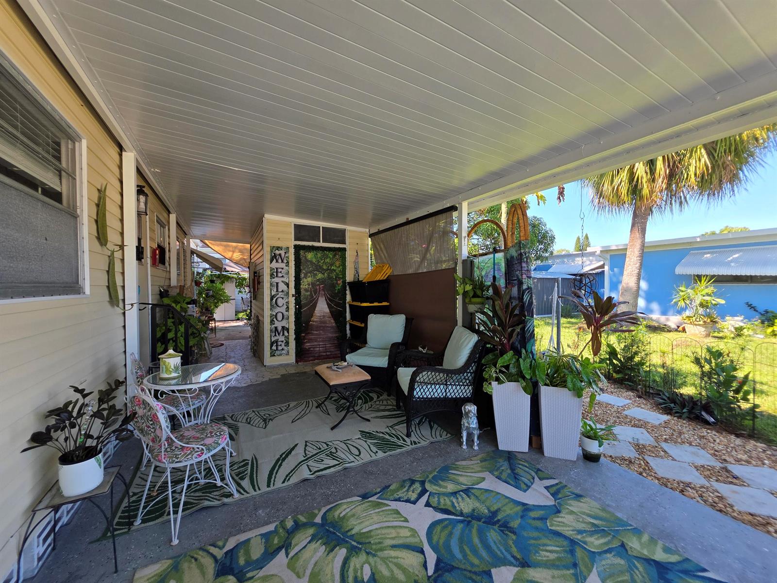 A covered patio features outdoor furniture, potted plants, and patterned rugs on a concrete floor — 6241 Elm Lane, Lantana FL 33462, LANTANA, FL