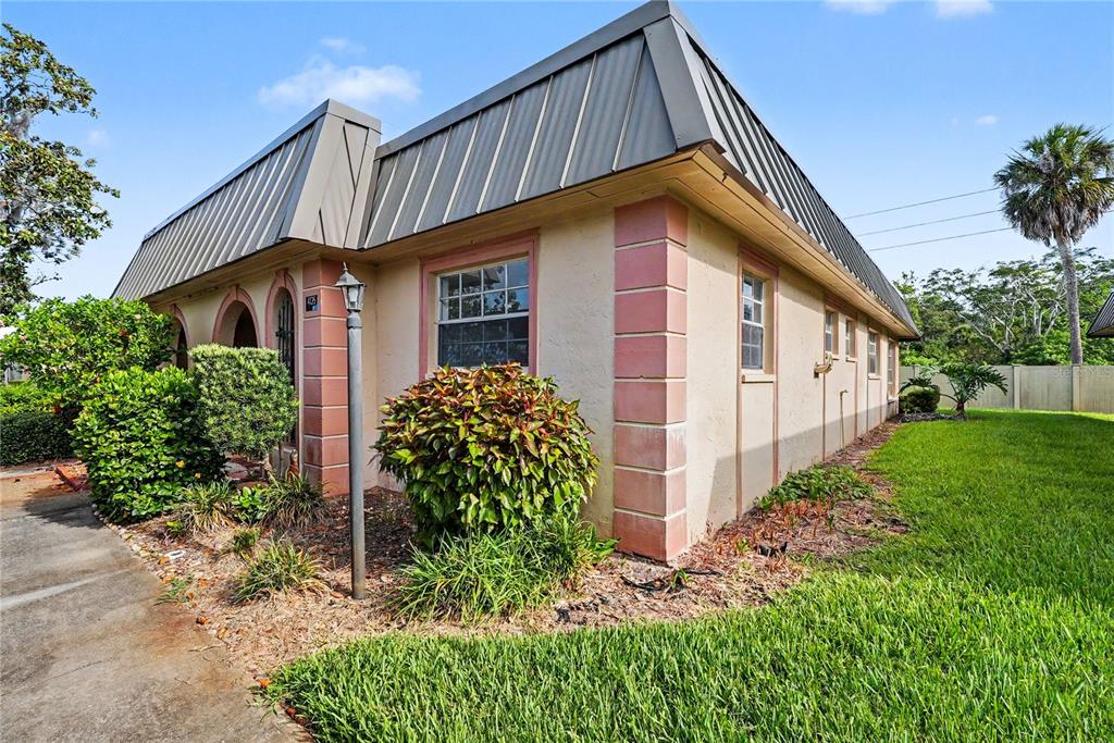 A single-story building with a metal mansard roof and pink corner accents sits on grass — 4135 STRATFORD DRIVE, NEW PORT RICHEY, FL