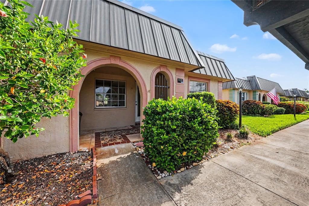 A tan stucco house with a metal roof and arched entryway features a front garden — 4135 STRATFORD DRIVE, NEW PORT RICHEY, FL