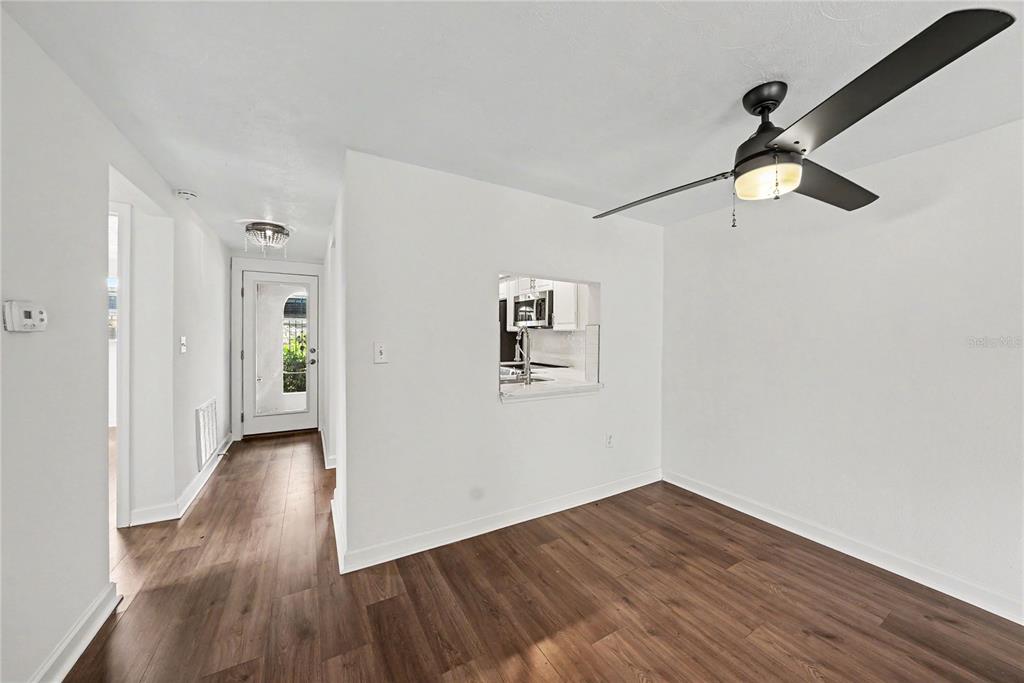 A room with wood-look flooring, a ceiling fan, and a pass-through window to the kitchen — 4135 STRATFORD DRIVE, NEW PORT RICHEY, FL