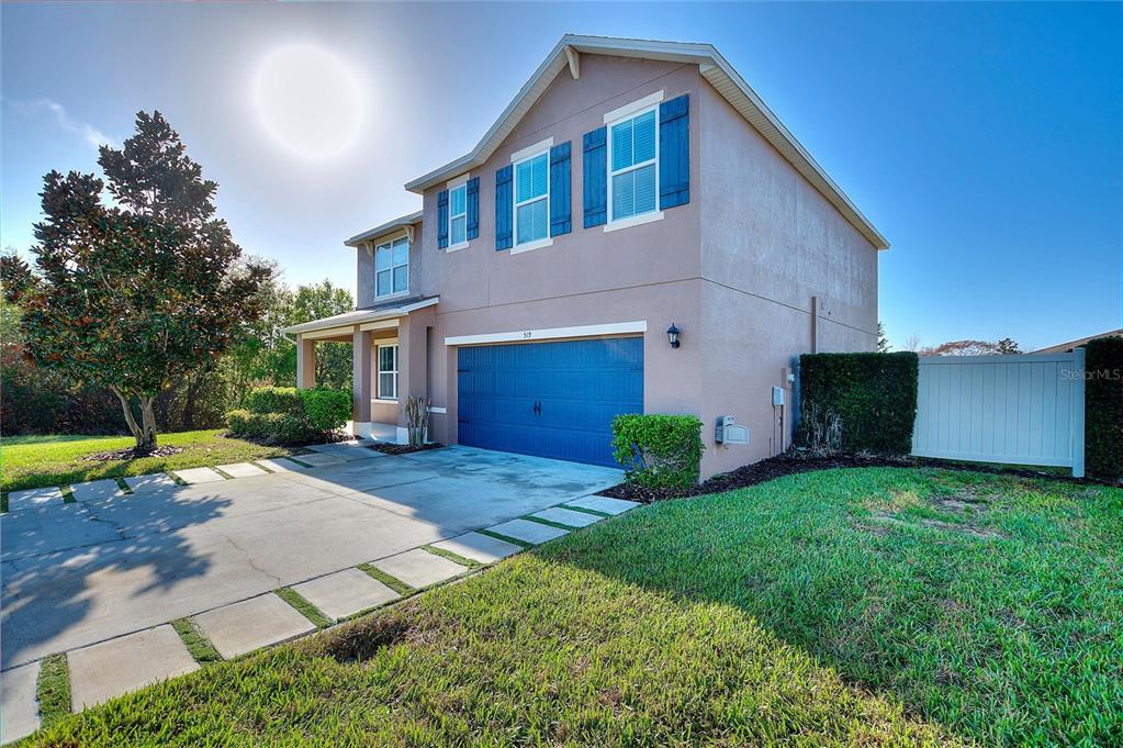 A two-story house with a blue garage door, beige stucco siding, and a concrete driveway — 519 OAKHURST WAY, LAKE ALFRED, FL