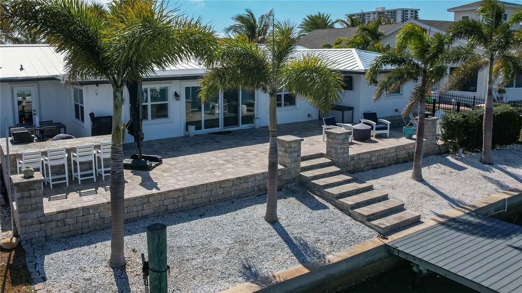 An elevated stone patio with outdoor seating overlooks a waterfront area with palm trees — 430 PALM ISLAND SE, CLEARWATER BEACH, FL