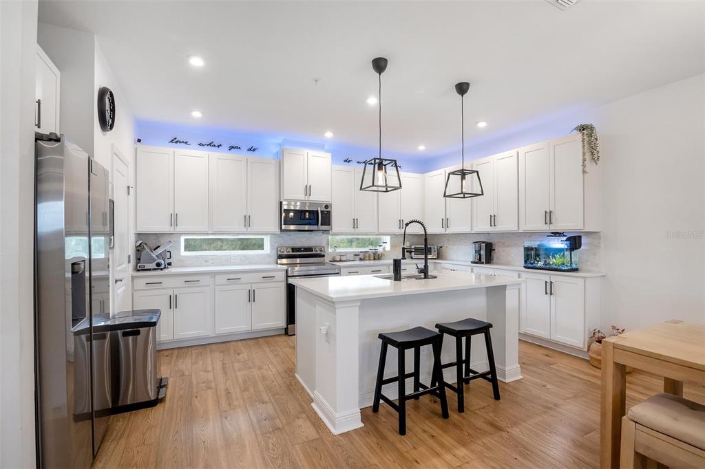 A white kitchen features a central island with bar stools and light wood flooring — 7251 NEMOURS PARKWAY, ORLANDO, FL