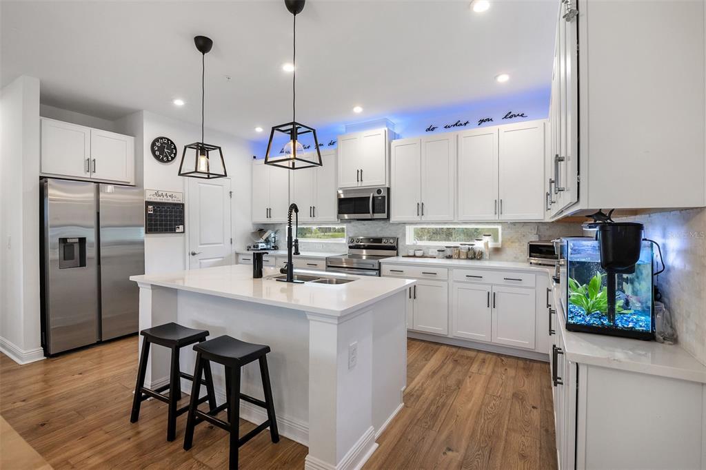 A modern kitchen features white cabinetry, stainless steel appliances, a central island, and wood flooring — 7251 NEMOURS PARKWAY, ORLANDO, FL