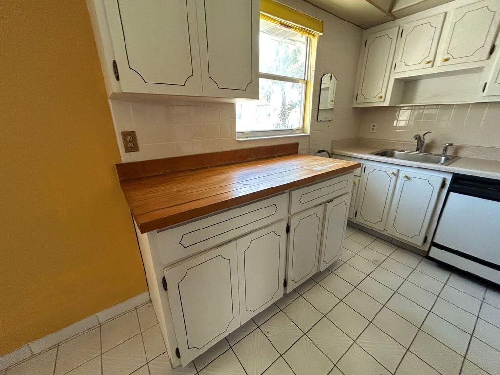 A kitchen features white cabinets, a wood countertop, a window, and white tiled flooring — 137 Saxony C Terrace, Delray Beach FL 33446, DELRAY BEACH, FL