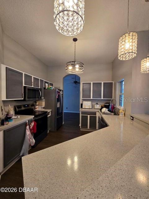 A kitchen features two-toned cabinetry, quartz countertops, and three decorative pendant lights hanging above — 1409 SUTTON ISLAND DRIVE, DELAND, FL