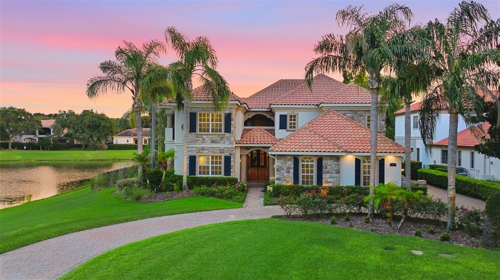 A two-story house with a tile roof, stone facade, and palm trees beside a lake — 6417 LAKE BURDEN VIEW DRIVE, WINDERMERE, FL