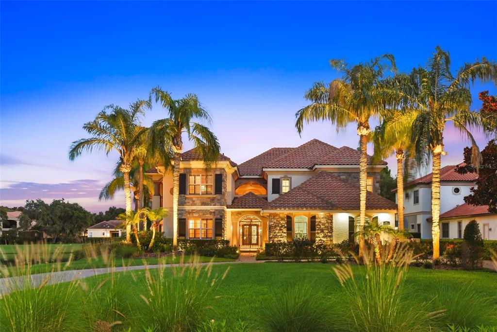 A two-story house with a stone facade, tile roof, and palm trees at dusk — 6417 LAKE BURDEN VIEW DRIVE, WINDERMERE, FL