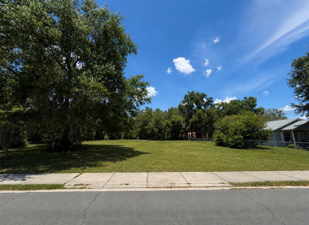 A vacant, grassy residential lot sits between mature trees and a neighboring house — 711 PINE, MOUNT DORA, FL