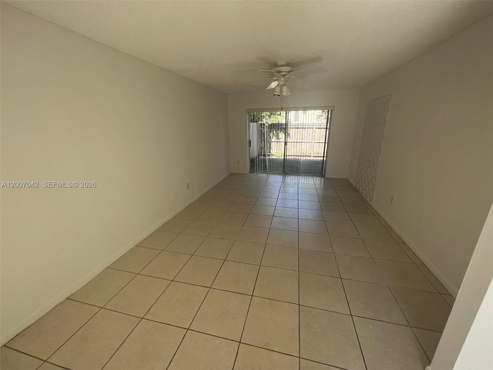 An empty room features beige tile flooring, a ceiling fan, and sliding glass doors — 11141 SW 70th Ter, Miami FL 33173, MIAMI, FL