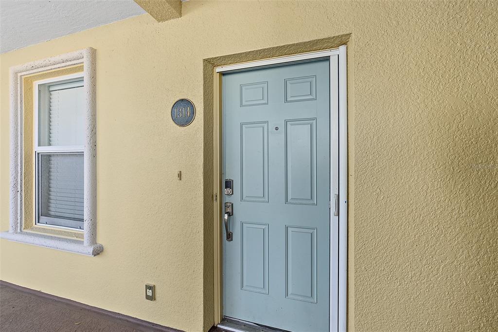 A light blue front door with a smart lock sits on a yellow exterior wall — 1300 CANOPY WALK LANE UNIT 1314, PALM COAST, FL