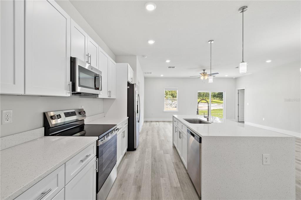 A modern kitchen features white cabinets, quartz countertops, stainless steel appliances, and light wood flooring — 2210 SW 149TH LANE, OCALA, FL