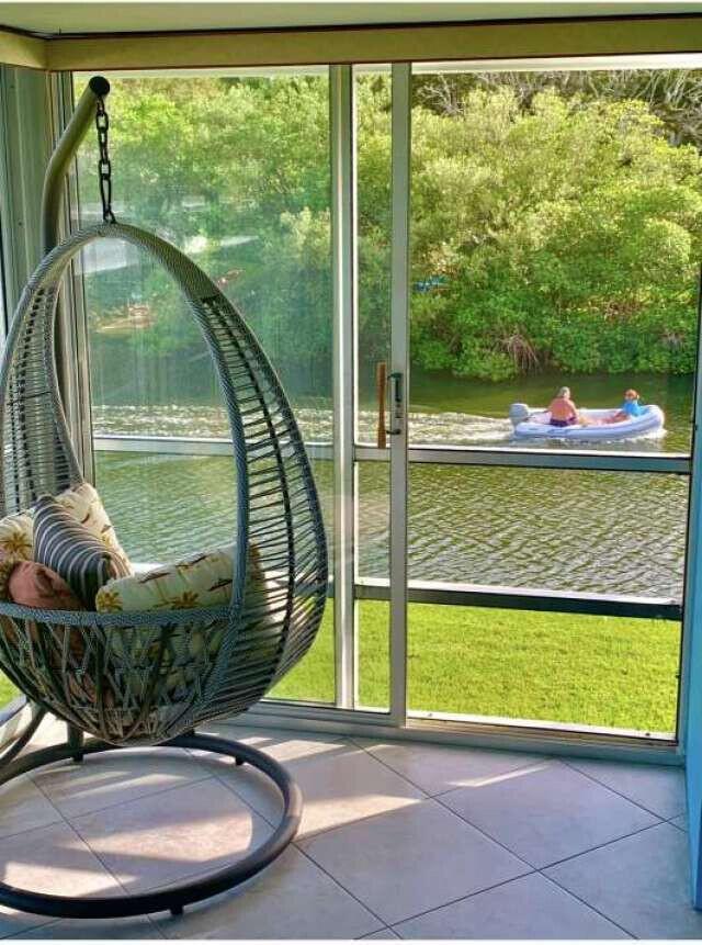 A hanging egg chair sits on a tiled porch overlooking a canal with a boat — 200 Greytwig Road # 213, Vero Beach FL 32963, VERO BEACH, FL