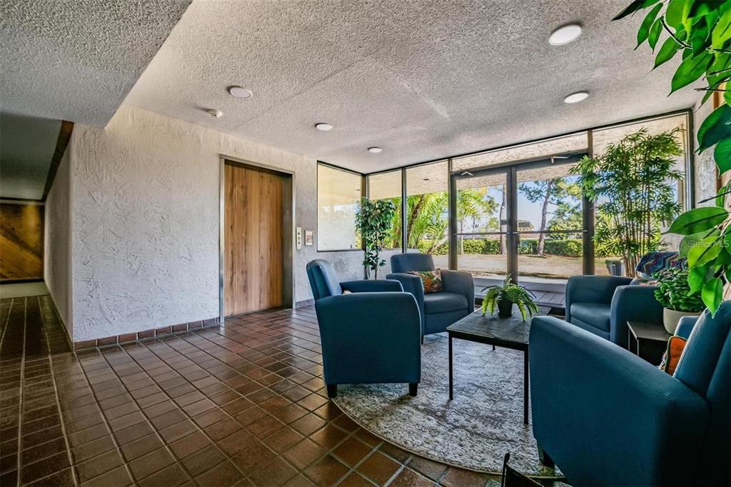 A lobby area features blue armchairs, a round rug, tile flooring, and glass exterior doors — 13602 S VILLAGE DRIVE UNIT 1106, TAMPA, FL
