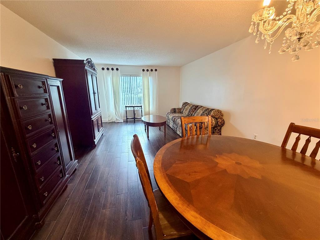 A dining area with a round wooden table leads into a living room with dark flooring — 13602 S VILLAGE DRIVE UNIT 1106, TAMPA, FL