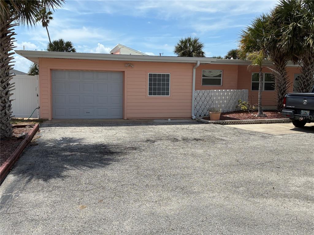 A peach-colored single-story house features a gray garage door and a gravel driveway — 3748 CARDINAL BOULEVARD, DAYTONA BEACH, FL
