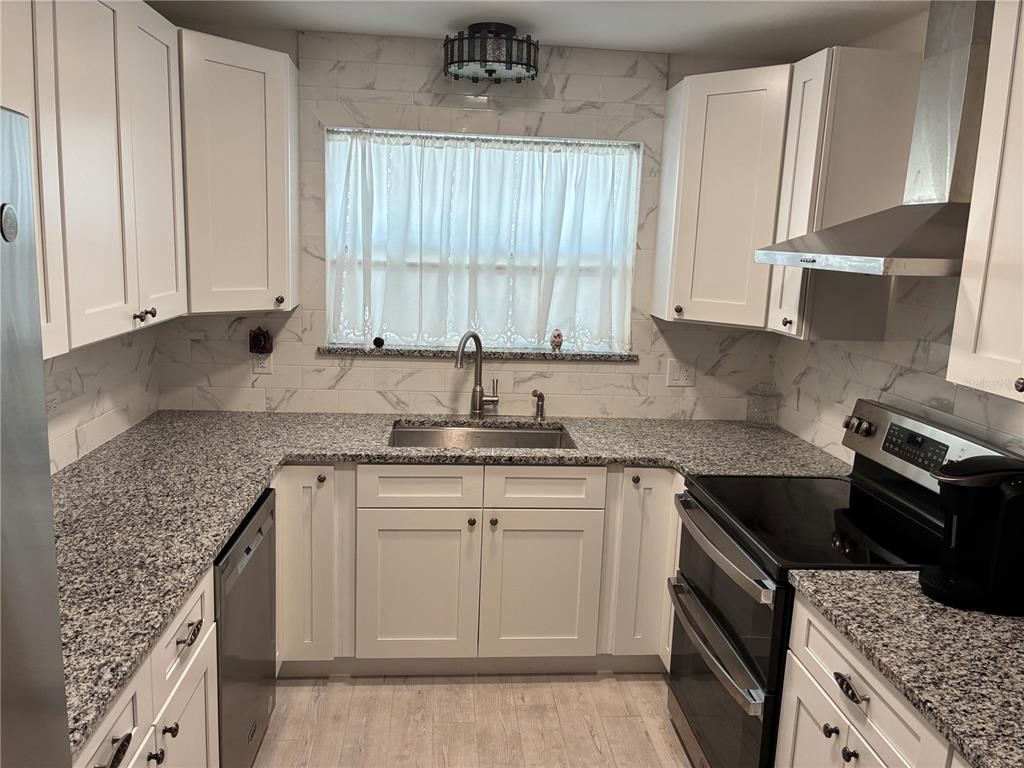 A kitchen features white cabinets, granite countertops, a stainless steel sink, and a tiled backsplash — 3748 CARDINAL BOULEVARD, DAYTONA BEACH, FL