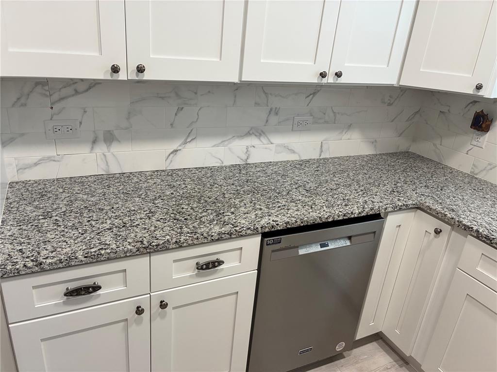 A kitchen features white cabinets, granite countertops, and a marble-look subway tile backsplash — 3748 CARDINAL BOULEVARD, DAYTONA BEACH, FL