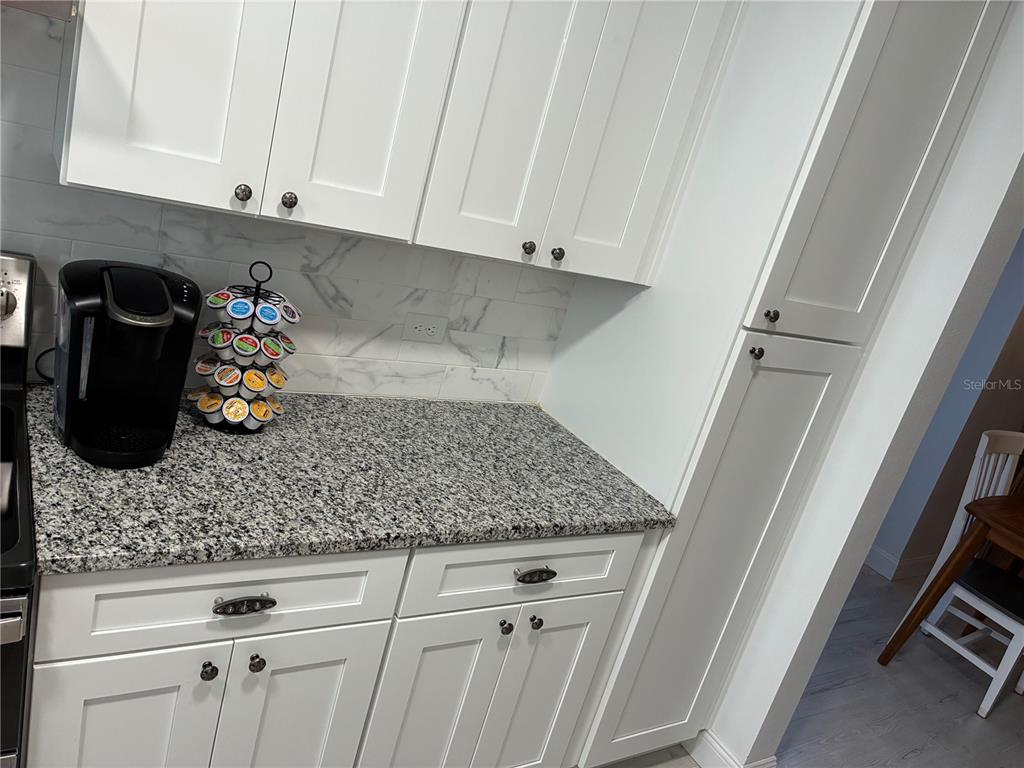 A kitchen features white cabinets, granite countertops, and a marble-style tile backsplash — 3748 CARDINAL BOULEVARD, DAYTONA BEACH, FL