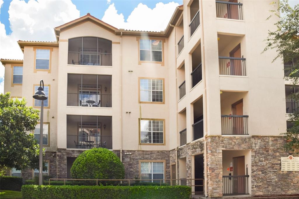 A multi-story apartment building features beige stucco walls, stone veneer accents, and screened-in balconies — 1375 TUSCANA LANE UNIT 1108, DAVENPORT, FL