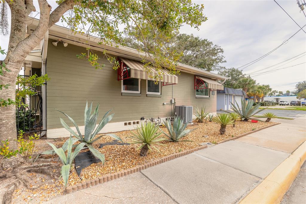 The exterior of a single-story building features olive green siding, striped awnings, and desert landscaping — 555 BALLOUGH ROAD, DAYTONA BEACH, FL