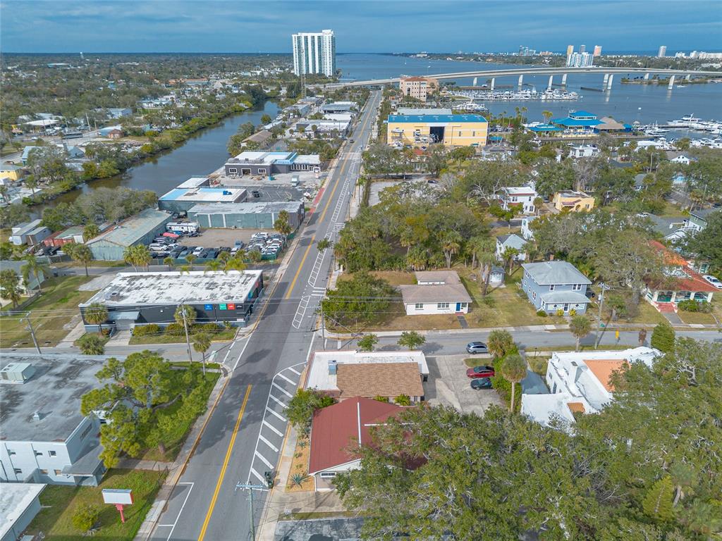 An aerial view shows a street running through a coastal town with buildings and water — 555 BALLOUGH ROAD, DAYTONA BEACH, FL