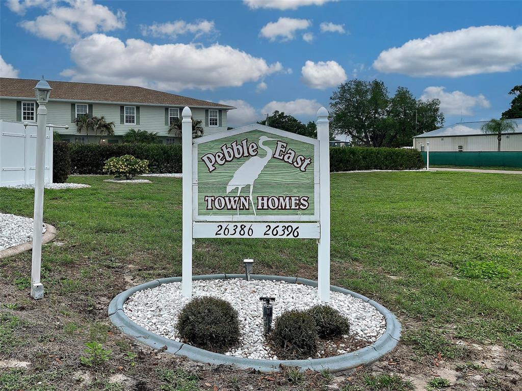 A sign for Pebble East Town Homes stands in a grassy yard before a building — 26396 NADIR ROAD UNIT 506, PUNTA GORDA, FL