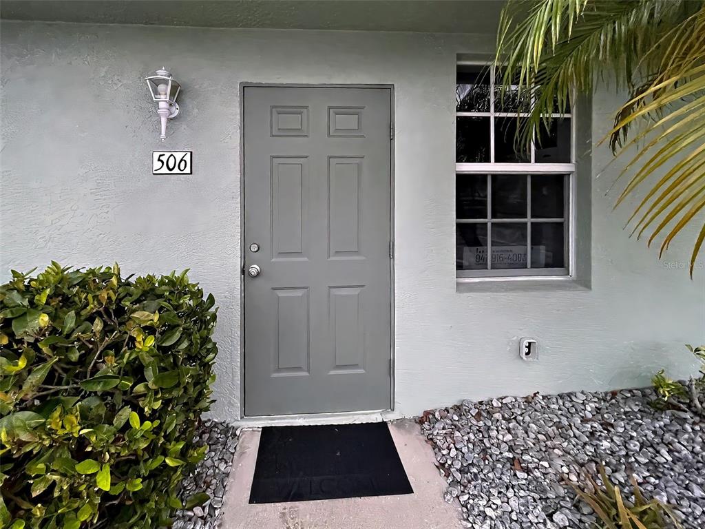 A gray front door with the number 506 is flanked by a bush and a window — 26396 NADIR ROAD UNIT 506, PUNTA GORDA, FL