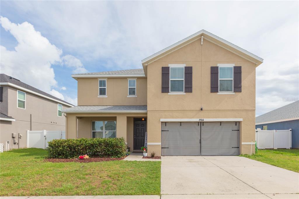 A two-story suburban house with a tan stucco exterior, a two-car garage, and a lawn — 3514 SAN MOISE PLACE, PLANT CITY, FL