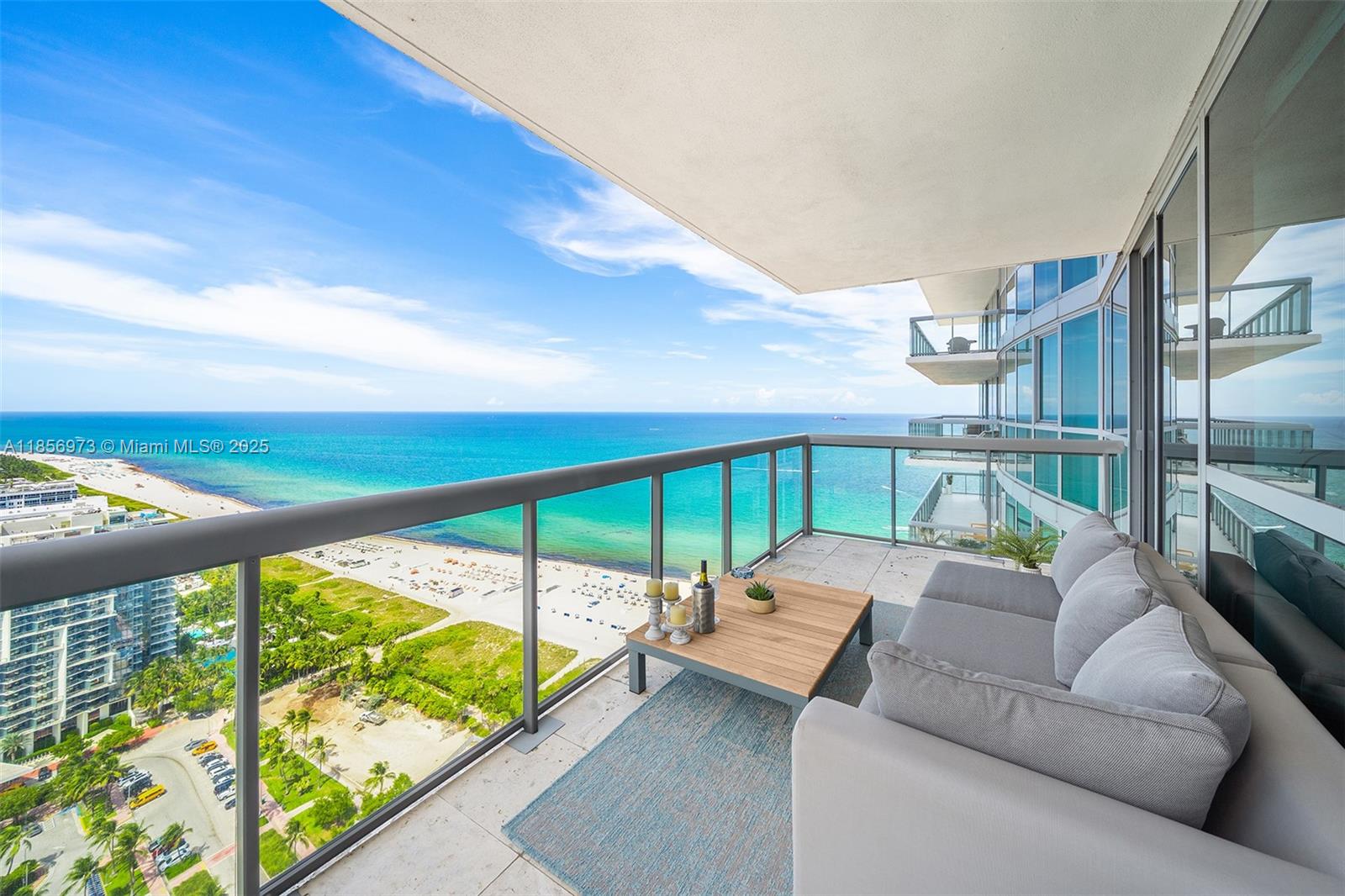 A balcony with a sofa and coffee table overlooks a beach and the ocean — 101 20th St # 3803, Miami Beach FL 33139, MIAMI BEACH, FL