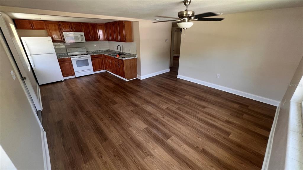 A kitchen with wood cabinets and white appliances opens into a living area with wood-look flooring — 2824 MEADOW VIEW AVENUE, LARGO, FL