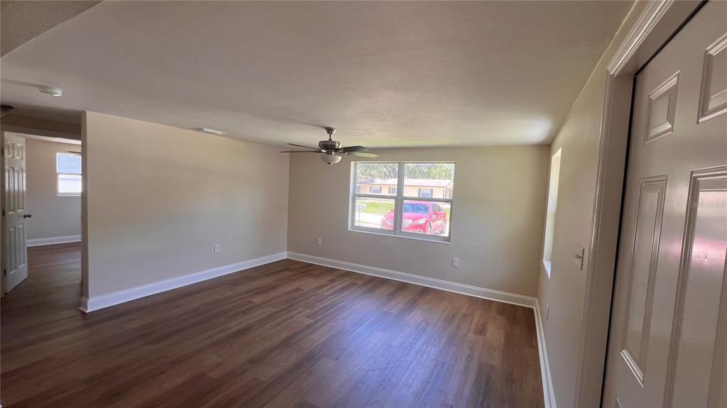 An empty room with wood-look flooring, beige walls, a ceiling fan, and a large window — 2824 MEADOW VIEW AVENUE, LARGO, FL